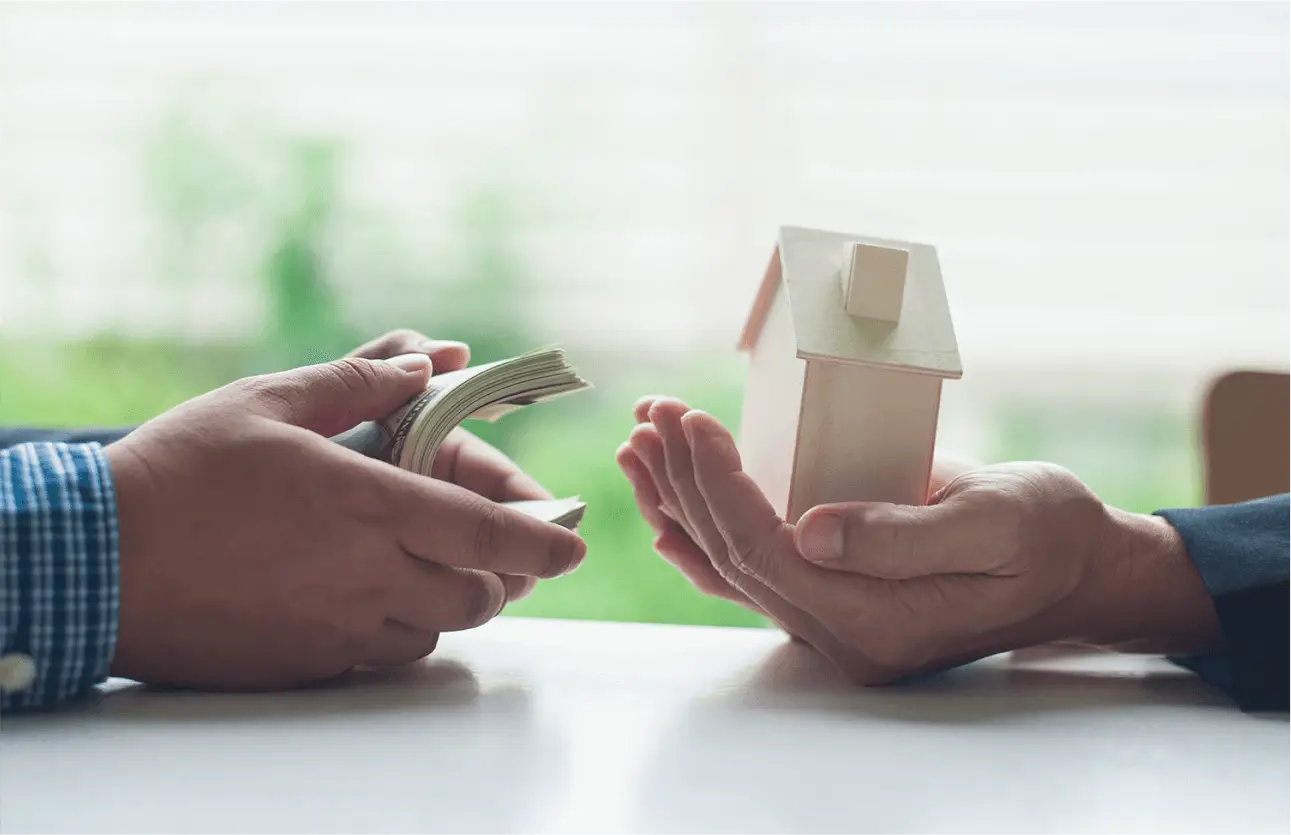 Two people exchanging money and a house model, illustrating negotiating with motivated sellers in real estate