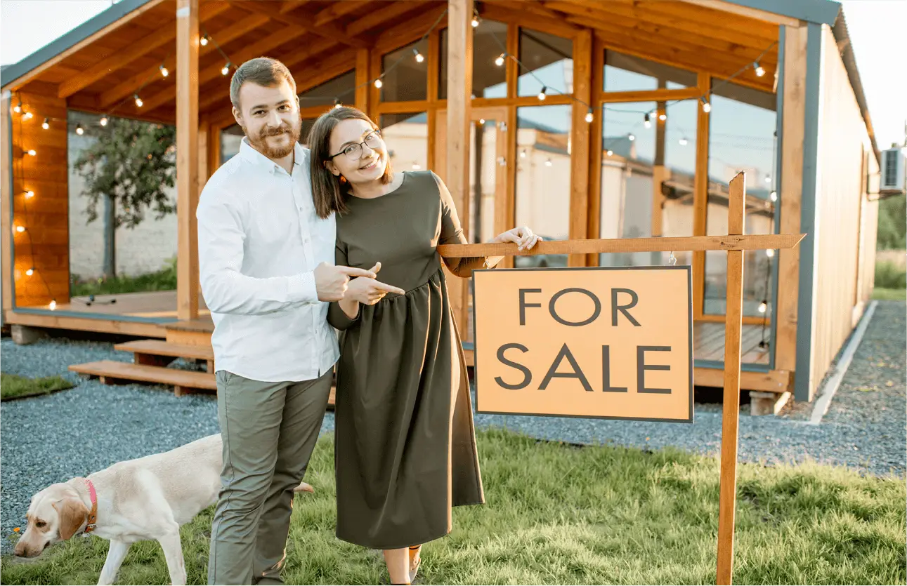 Homeowners standing by a for-sale sign, representing motivated seller leads in the real estate market