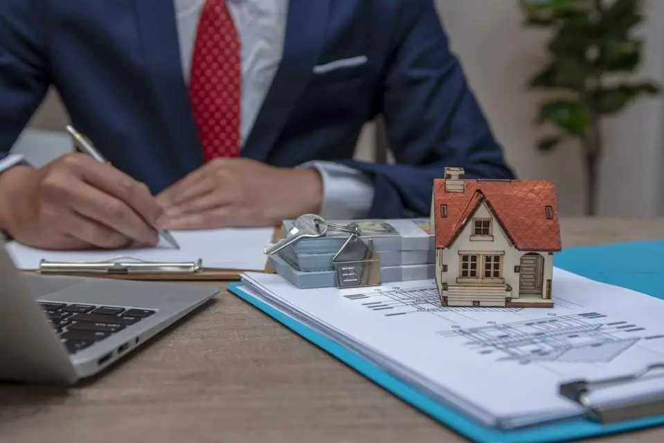 Real estate investor reviewing property documents with a model house and contract materials on the desk, illustrating real estate wholesaling.